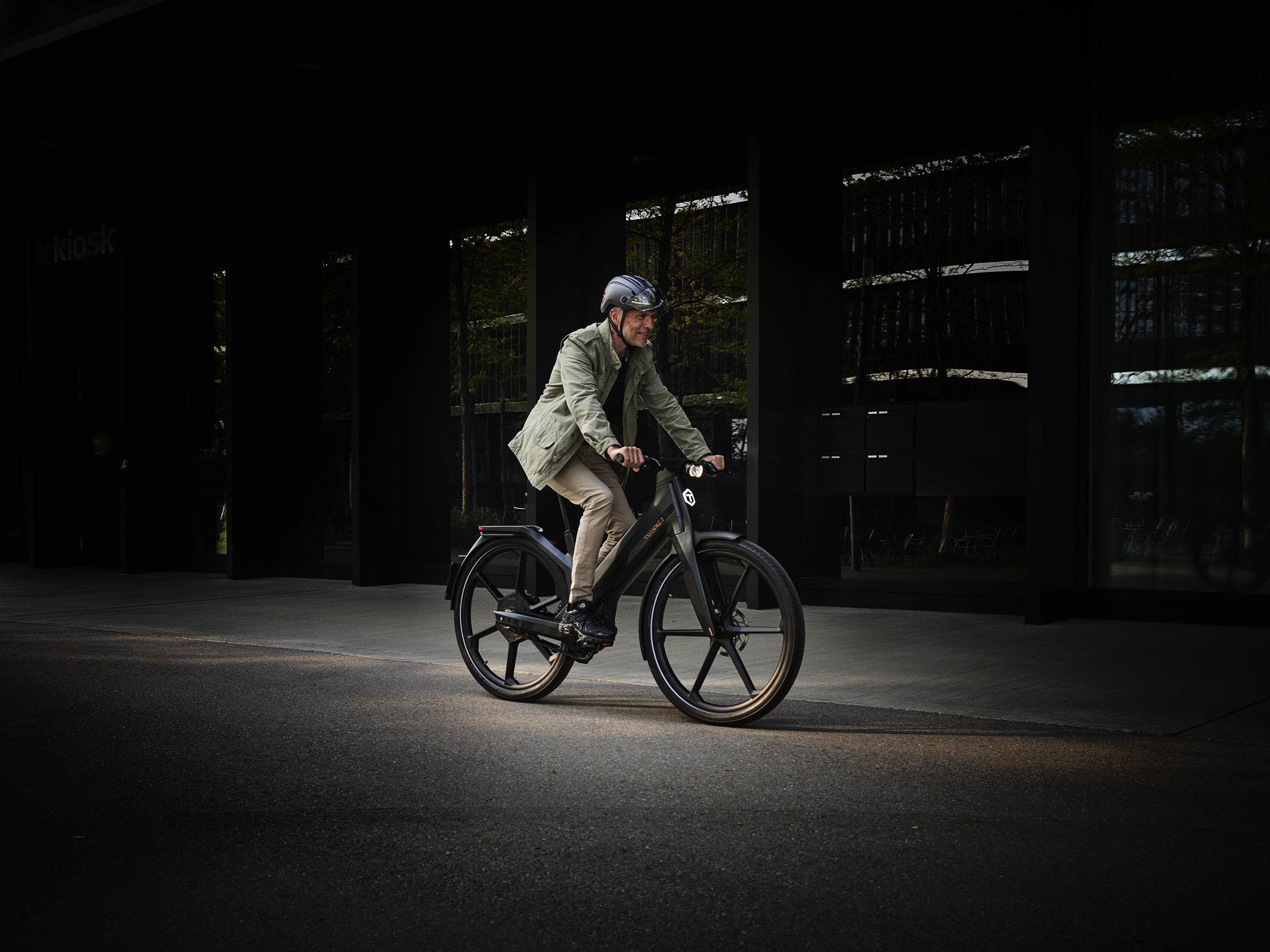 A man rides through the city on a Twinner. The black bike is illuminated.